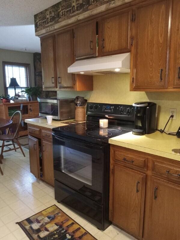 1361 E Dunkirk St, Springfield, MO 65804 - kitchen with black range with electric stovetop, ventilation hood, light countertops, stainless steel microwave, and brown cabinets