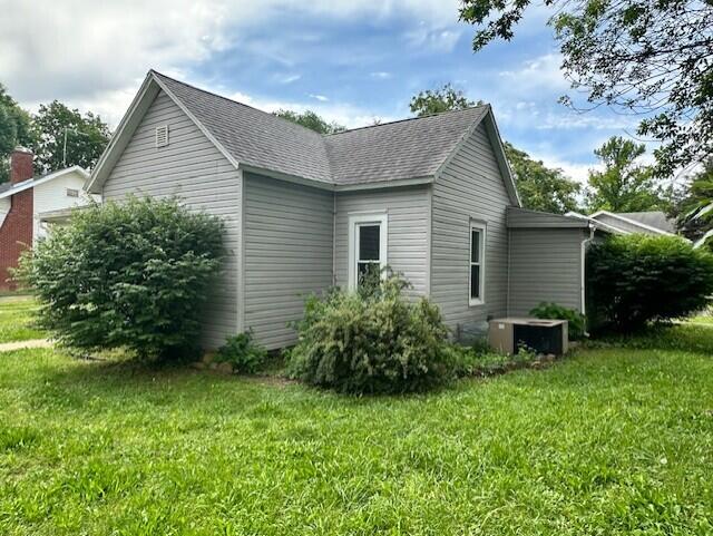 627 W Cherry St, Nevada, MO 64772 - view of side of home featuring a lawn, central AC unit, and a shingled roof