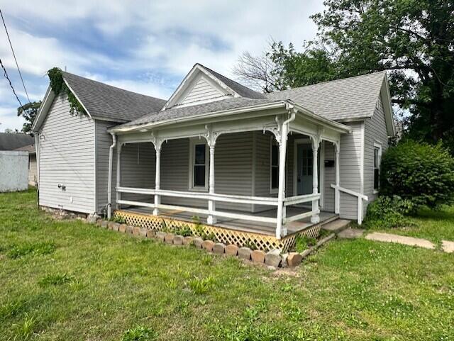 627 W Cherry St, Nevada, MO 64772 - view of home's exterior with a porch, roof with shingles, and a lawn