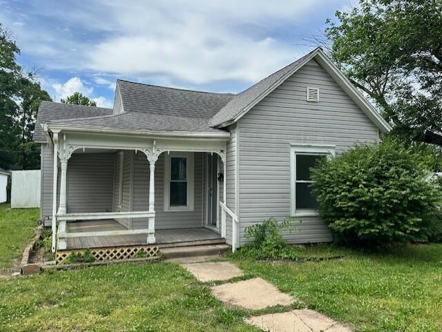 627 W Cherry St, Nevada, MO 64772 - view of front facade with a porch, a front yard, and a shingled roof