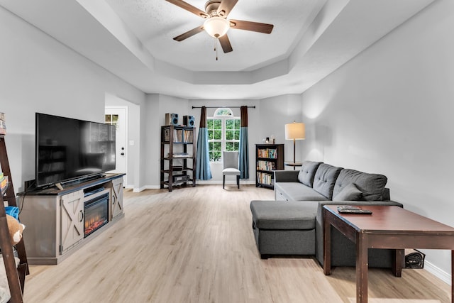 1108 E Robin St, Ozark, MO 65721 - living room with a ceiling fan, light wood-type flooring, a tray ceiling, a glass covered fireplace, and baseboards
