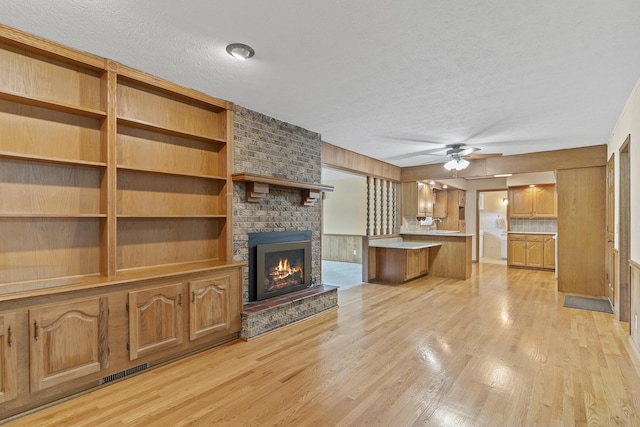 5263 N Crestwood Dr, Springfield, MO 65803 - unfurnished living room featuring a textured ceiling, a brick fireplace, light wood-style floors, and ceiling fan