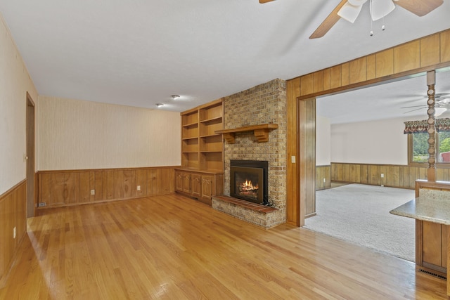 5263 N Crestwood Dr, Springfield, MO 65803 - unfurnished living room featuring light wood-type flooring, wooden walls, a ceiling fan, wainscoting, and a fireplace