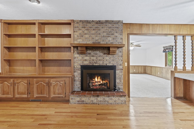5263 N Crestwood Dr, Springfield, MO 65803 - unfurnished living room with a textured ceiling, light wood-type flooring, a brick fireplace, wood walls, and wainscoting