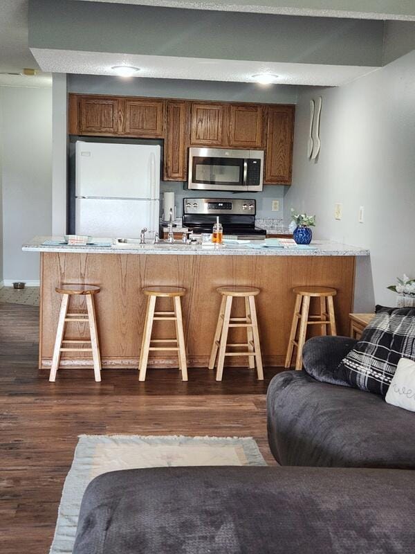 388 Notch Ln Unit 12, Branson West, MO 65737 - kitchen featuring appliances with stainless steel finishes, brown cabinetry, dark wood-style flooring, and a kitchen bar