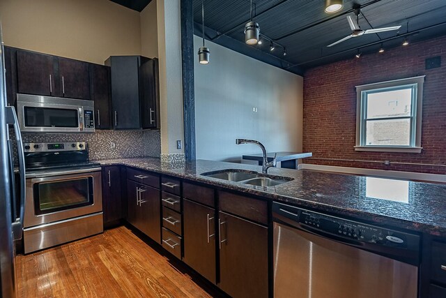 kitchen featuring appliances with stainless steel finishes, a sink, light wood finished floors, dark stone countertops, and brick wall