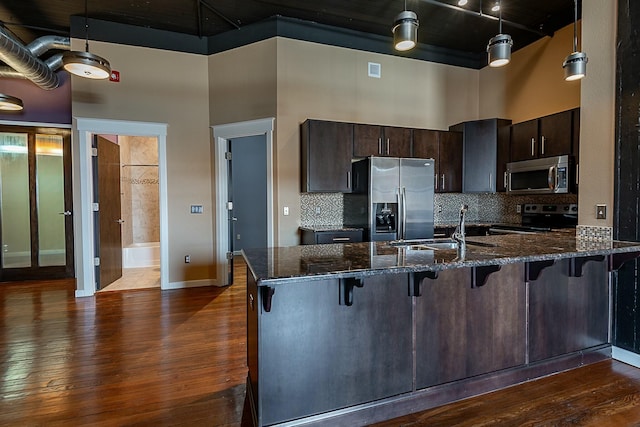 kitchen featuring appliances with stainless steel finishes, a towering ceiling, a sink, dark wood-type flooring, and dark brown cabinets