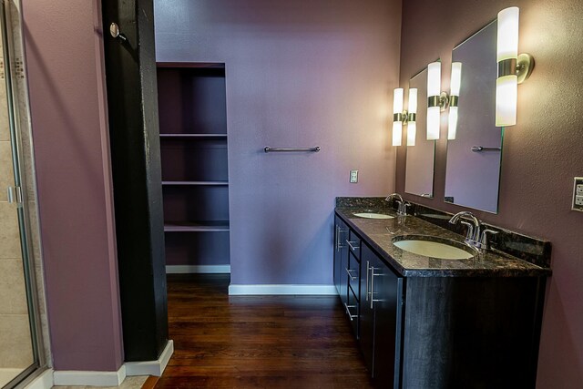 bathroom featuring wood finished floors, double vanity, baseboards, and a shower with door