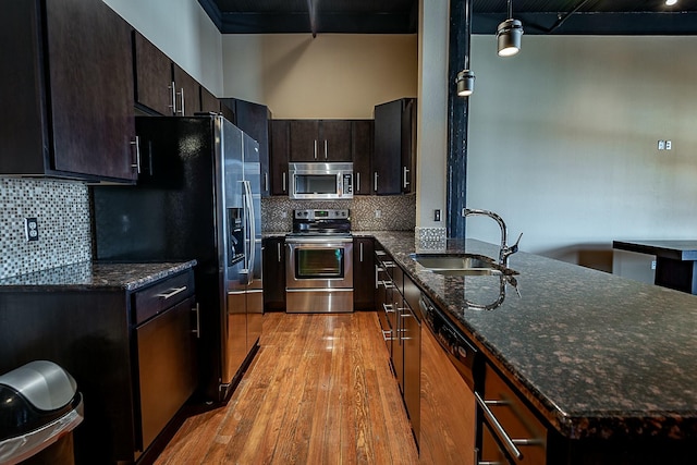 kitchen featuring stainless steel appliances, a sink, light wood-style floors, and backsplash
