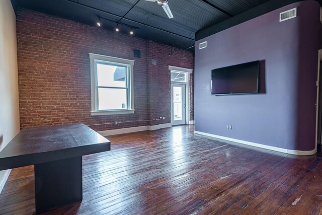 unfurnished living room featuring wood-type flooring, baseboards, track lighting, brick wall, and arched walkways