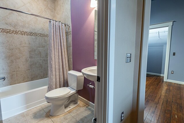 bathroom featuring toilet, shower / bath combination with curtain, a sink, baseboards, and wood-type flooring