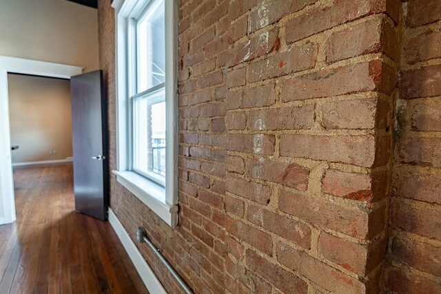 hallway featuring hardwood / wood-style flooring, baseboards, and brick wall