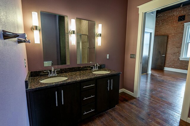 full bathroom with wood-type flooring, baseboards, double vanity, and brick wall
