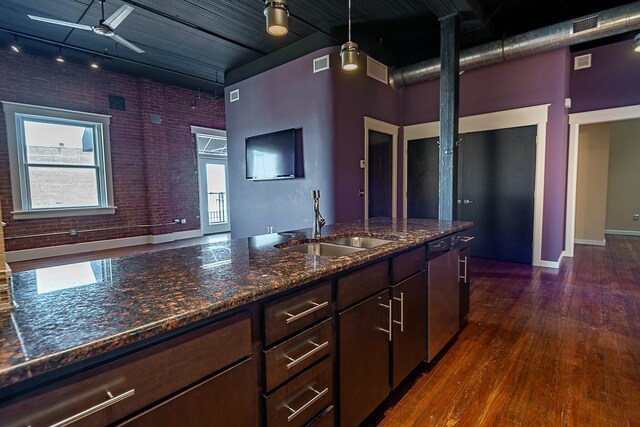 kitchen featuring stainless steel dishwasher, a sink, brick wall, a ceiling fan, and dark wood-type flooring