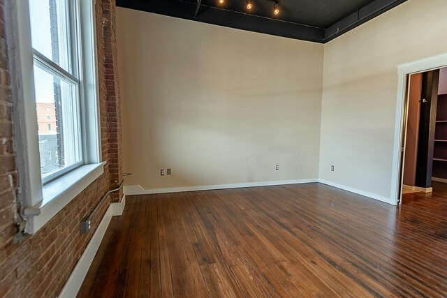 unfurnished room with dark wood-style flooring, brick wall, baseboards, and a towering ceiling