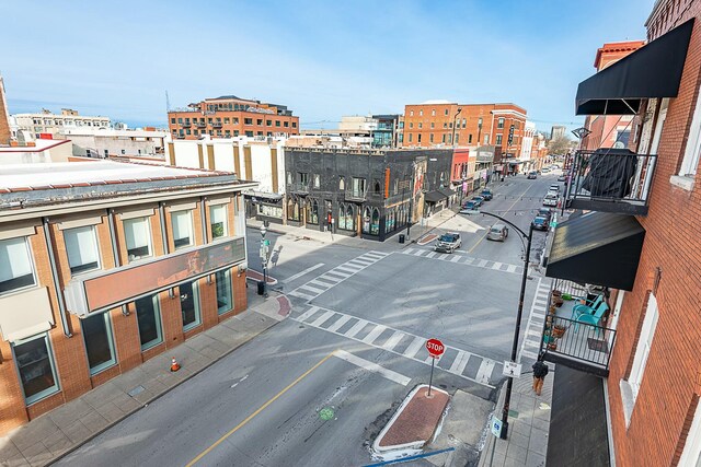view of asphalt road with sidewalks, traffic signs, curbs, street lights, and a city view