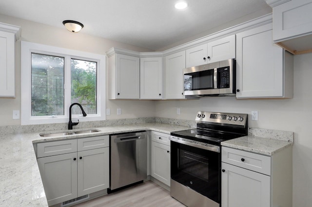 1436 W Whiteside St, Springfield, MO 65807 - kitchen with stainless steel appliances, a sink, light wood-style floors, white cabinets, and light stone counters