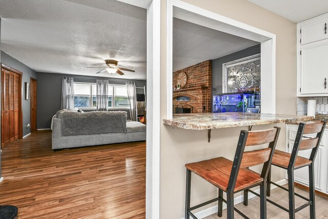 2052 N Grant Ave, Springfield, MO 65803 - kitchen featuring wood finished floors, white cabinetry, a ceiling fan, a breakfast bar area, and a brick fireplace