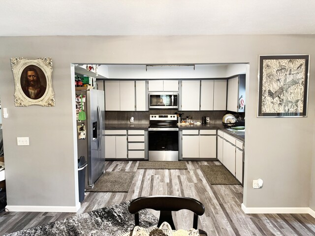 27641 County Road 356, Pittsburg, MO 65724 - kitchen featuring stainless steel appliances, dark countertops, light wood finished floors, decorative backsplash, and baseboards