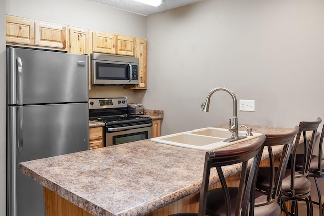550 Notch Ln Unit 2, Reeds Spring, MO 65737 - kitchen featuring appliances with stainless steel finishes, light brown cabinetry, a sink, a kitchen breakfast bar, and a textured ceiling