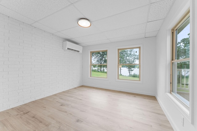26237 Twin Rivers Dr, Shell Knob, MO 65747 - empty room with brick wall, a drop ceiling, a wall mounted air conditioner, and light wood-style flooring