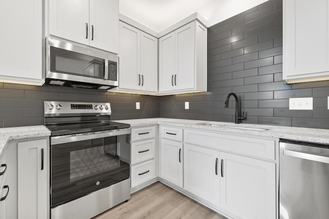 228 Vacation Ln Unit 2, Reeds Spring, MO 65737 - kitchen with stainless steel appliances, a sink, tasteful backsplash, white cabinetry, and light wood finished floors