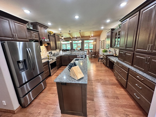 1762 Hickory Ridge Cir, Nixa, MO 65714 - kitchen featuring appliances with stainless steel finishes, a peninsula, light wood-style floors, an island with sink, and light stone counters