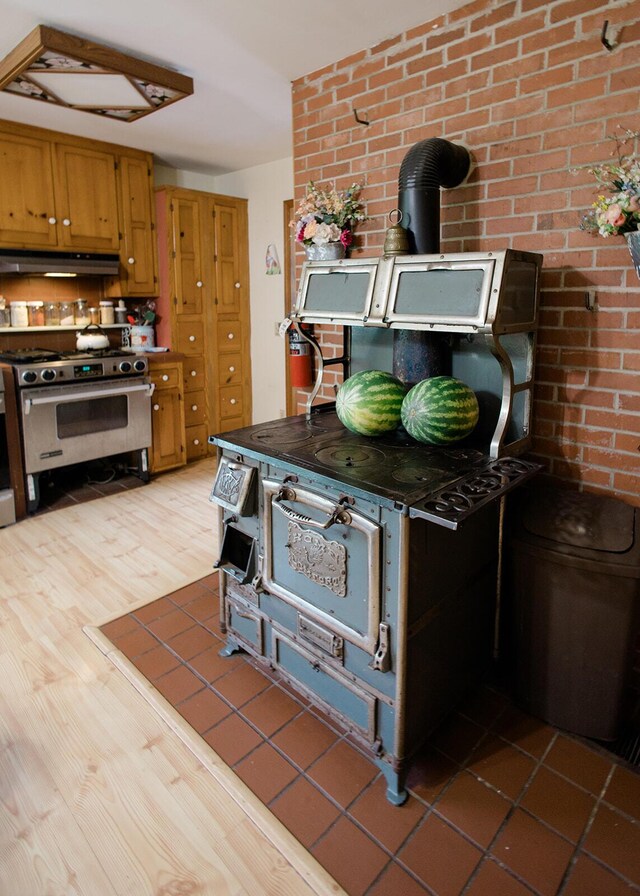 19429 E State Highway 14, Ava, MO 65608 - kitchen featuring high end stainless steel range oven, under cabinet range hood, light wood-style flooring, brown cabinets, and brick wall