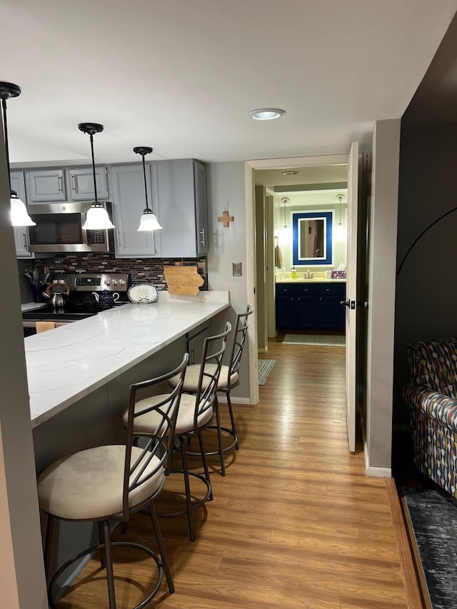 234 Sunset Cv Unit 107, Branson, MO 65616 - kitchen with stainless steel microwave, range with electric cooktop, light wood-style floors, tasteful backsplash, and a kitchen bar