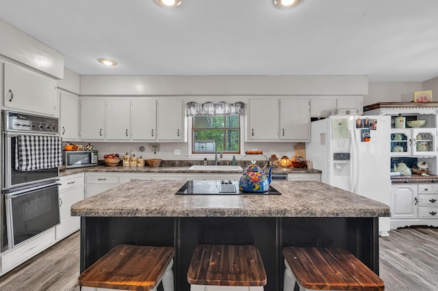 21371 Howell Rd, Mountain View, MO 65548 - kitchen with black appliances, a sink, a kitchen bar, white cabinets, and light wood-style flooring