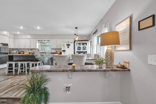 21371 Howell Rd, Mountain View, MO 65548 - kitchen with stainless steel microwave, white refrigerator with ice dispenser, a kitchen breakfast bar, white cabinetry, and a peninsula