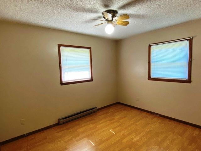 1208 Oak Ridge Dr, Aurora, MO 65605 - empty room featuring a baseboard heating unit, light wood-style floors, ceiling fan, baseboards, and a textured ceiling