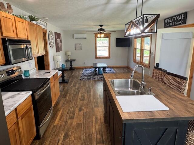 83 Dawn Cir, Galena, MO 65656 - kitchen with appliances with stainless steel finishes, a wall mounted AC, dark wood-type flooring, a ceiling fan, and a kitchen island with sink