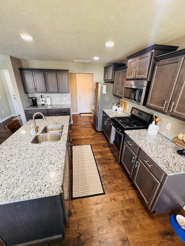 607 E Selby Dr, Nixa, MO 65714 - kitchen featuring stainless steel appliances, dark wood-style flooring, a center island with sink, light stone countertops, and decorative backsplash