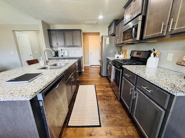 607 E Selby Dr, Nixa, MO 65714 - kitchen with appliances with stainless steel finishes, dark wood-style floors, a kitchen island with sink, tasteful backsplash, and light stone countertops