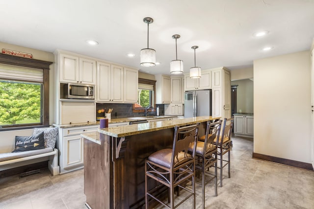 1029 Riverview Rd, Clever, MO 65631 - kitchen featuring appliances with stainless steel finishes, cream cabinetry, light stone counters, a kitchen island, and tasteful backsplash