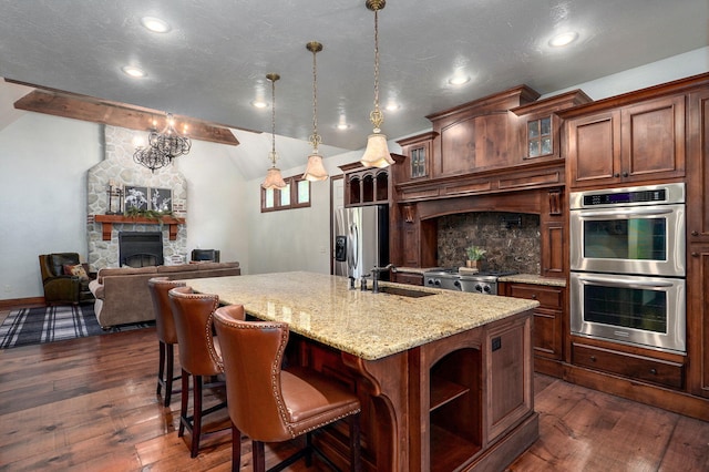 7607 N Angler Ln, Strafford, MO 65757 - kitchen with appliances with stainless steel finishes, a stone fireplace, dark wood finished floors, an island with sink, and glass insert cabinets