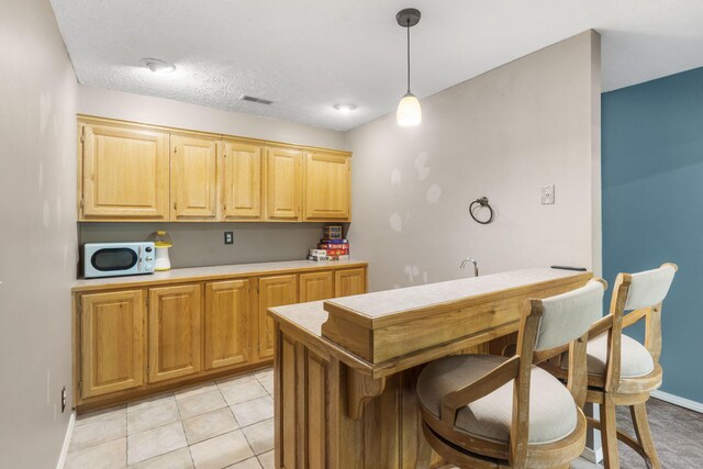 2504 W Fox Fire Ct, Nixa, MO 65714 - kitchen with white microwave, hanging light fixtures, light countertops, light brown cabinetry, and light tile patterned floors