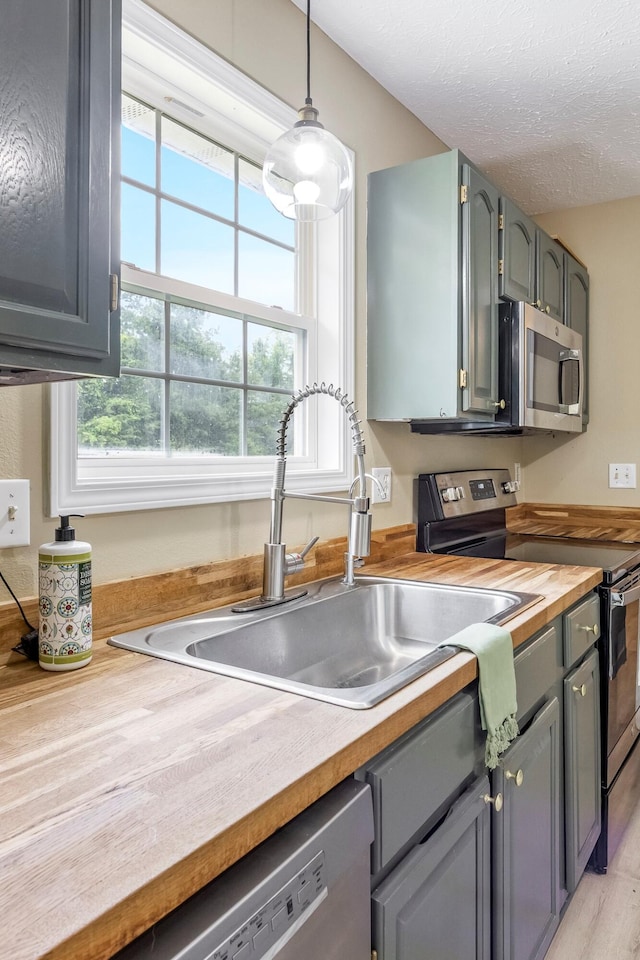3936 S 77th Rd, Dunnegan, MO 65640 - kitchen featuring appliances with stainless steel finishes, butcher block counters, decorative light fixtures, gray cabinetry, and a textured ceiling