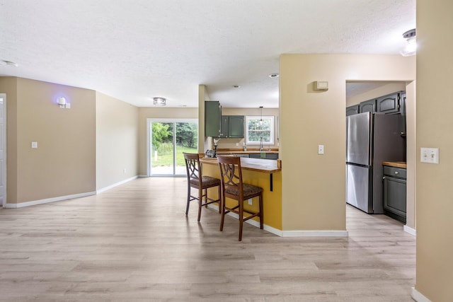 3936 S 77th Rd, Dunnegan, MO 65640 - kitchen with freestanding refrigerator, light wood-type flooring, a textured ceiling, a breakfast bar, and green cabinets