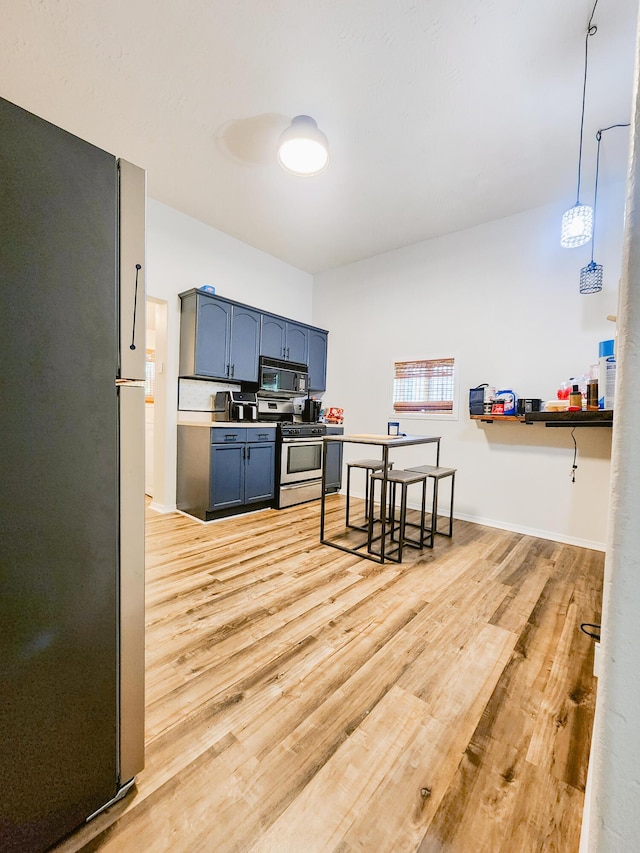 1305 N Main Ave, Springfield, MO 65802 - kitchen featuring stainless steel range with gas cooktop, freestanding refrigerator, black microwave, light wood finished floors, and blue cabinetry