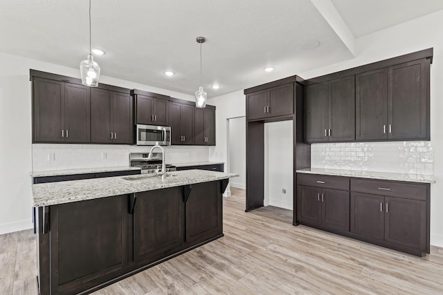 1305 W Ragweed Ct, Ozark, MO 65721 - kitchen featuring stainless steel microwave, decorative backsplash, dark brown cabinets, pendant lighting, and light wood-type flooring