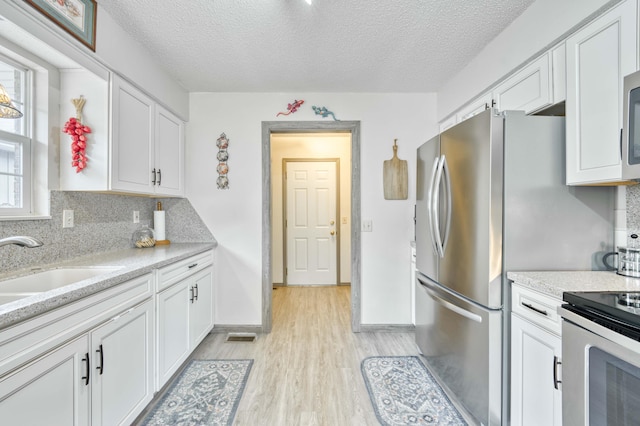 202 N Harper Ave, Springfield, MO 65802 - kitchen featuring appliances with stainless steel finishes, light wood-style floors, white cabinets, tasteful backsplash, and a textured ceiling