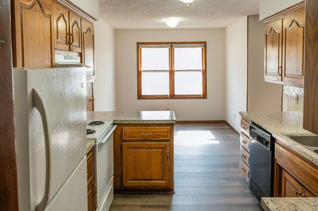 2812 W Maplewood St, Springfield, MO 65807 - kitchen featuring white appliances, a peninsula, dark wood-style floors, extractor fan, and brown cabinets