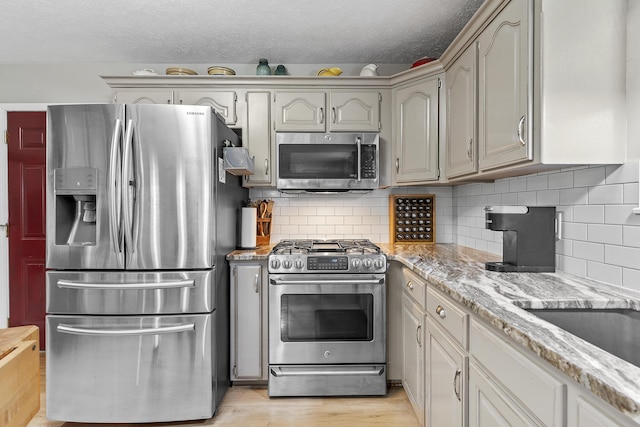 11996 N Farm Rd Unit 119, Brighton, MO 65617 - kitchen featuring appliances with stainless steel finishes, a textured ceiling, light wood-style flooring, tasteful backsplash, and light stone counters