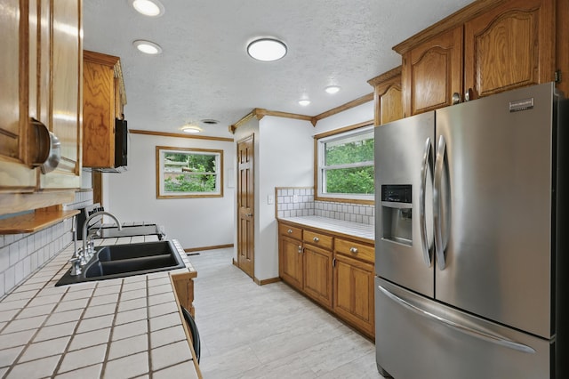 14289 Bethel Rd, Seneca, MO 64865 - kitchen featuring stainless steel fridge, tile countertops, backsplash, crown molding, and brown cabinetry