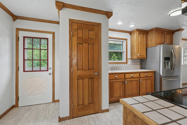 14289 Bethel Rd, Seneca, MO 64865 - kitchen featuring stainless steel fridge with ice dispenser, tile counters, brown cabinets, ornamental molding, and tasteful backsplash