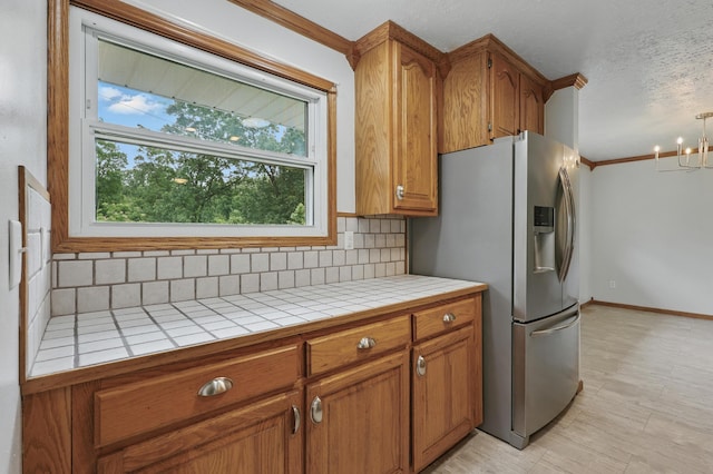 14289 Bethel Rd, Seneca, MO 64865 - kitchen featuring tile counters, stainless steel fridge with ice dispenser, backsplash, brown cabinets, and a chandelier