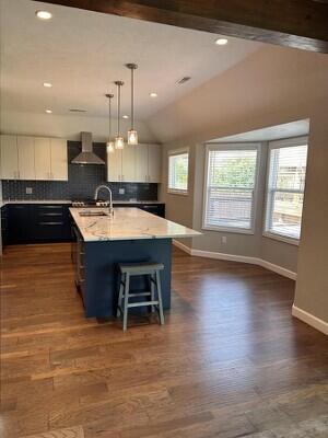 201 Sparrow Ln, Willard, MO 65781 - kitchen with wall chimney range hood, vaulted ceiling, white cabinetry, a center island with sink, and decorative backsplash