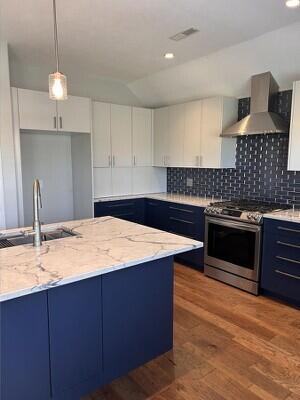 201 Sparrow Ln, Willard, MO 65781 - kitchen featuring stainless steel gas range, wall chimney exhaust hood, blue cabinets, light stone counters, and white cabinets